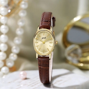 Elegant gold oval watch with brown leather strap and pearl jewelry accessories