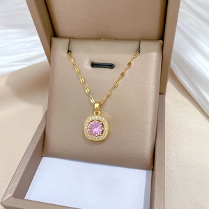 Detail of a gold titanium necklace with a square pink gemstone pendant in a jewelry box