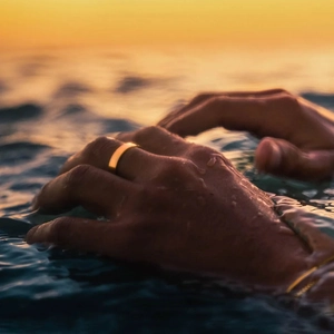 Close-up of golden minimalist stainless steel ring on hand submerged in water drops