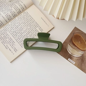 Dettaglio della pinza per capelli rettangolare verde scuro opaco su sfondo minimalista