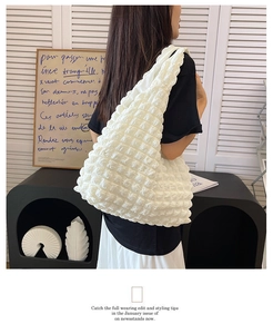 Detail of white pleated bubble texture shoulder bag shown on model in minimalist setting