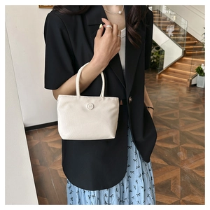 Détail d'un sac seau en nylon crème avec une boucle ronde m porté par un mannequin