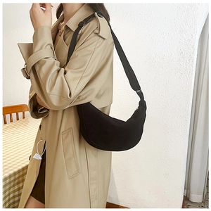 Model wearing a black corduroy crescent crossbody bag with a trench coat in a cozy room