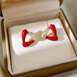 Détail de boucles d'oreilles triangle en émail rouge et zircons dans un coffret vert