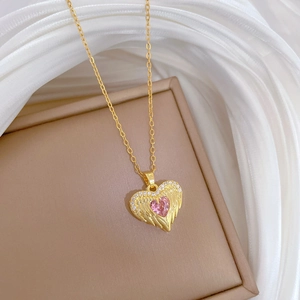 Macro detail of a gold angel wing necklace with a pink heart gemstone on a jewelry box