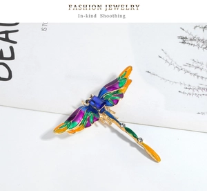 Macro detail of enamel dragonfly brooch with vibrant colored wings and a blue center gemstone