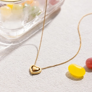 Detail of 18K gold stainless steel necklace with double heart pendant on stone surface