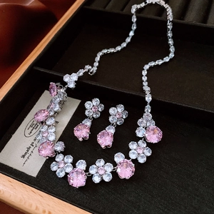 Detailed close-up of pink zircon flower pendant necklace and earrings set in a velvet box