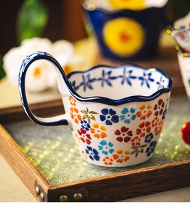 Macro detail of hand-painted floral ceramic mug with wavy rim and elegant blue handle