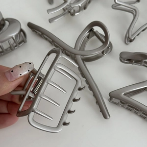 Close-up of matte silver metal hair claw clips in various shapes on a white surface