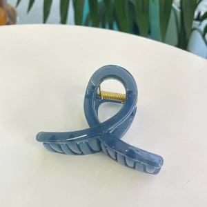 Détail d'une pince à cheveux en acrylique bleu avec ressort en métal doré sur fond blanc