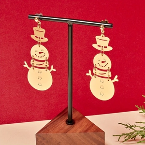 Golden minimalist hollow snowman earrings on a black display stand with festive red background