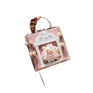Sac boîte rose avec reliefs de roses blanches et bandoulière en perles sur fond blanc