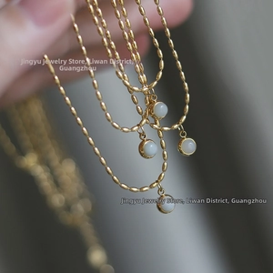 Close-up of golden beaded chain necklace with four round white stone pendants