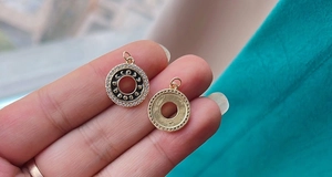 Macro detail of a round gold charm with black enamel, sparkling stones and star motifs