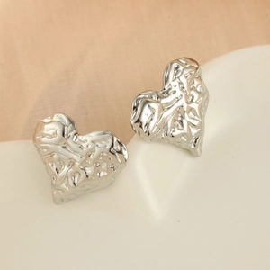 Vue macro de clous d'oreilles cœur argentés avec texture métallique plissée et design unique