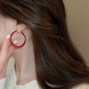 Close-up of model wearing large red enamel hoop earrings in a retro minimalist style