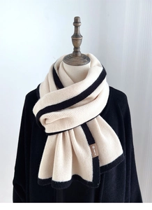 Detail of beige knitted scarf with black trim showing texture and brand label