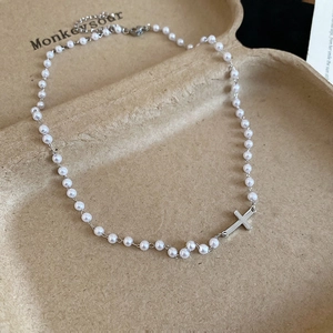 Close-up of pearl necklace featuring a silver cross pendant and adjustable clasp