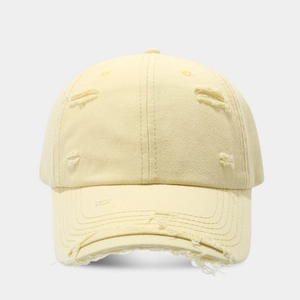 Close-up detail of distressed distressed holes and frayed edges on the cream cotton baseball cap