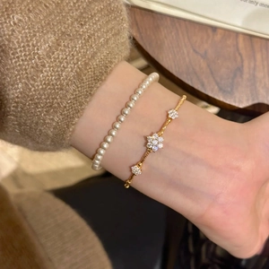 Detail of layered gold floral bracelet and white pearl bracelet on a model wrist