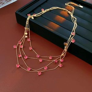 Détail macro du collier multicouche doré avec gemmes roses sur plateau velours