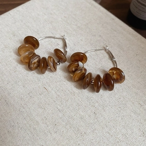 Detail of amber resin bead hoop earrings on beige linen fabric with silver needles