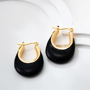 Detailed close-up of U-shaped gold earrings with black enamel on a white geometric stand