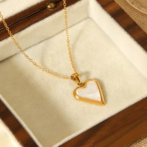 Golden heart pendant necklace with white shell inlay displayed in a wooden jewelry box