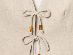 Détail d'un haut en lin beige avec des nœuds délicats et des perles ambrées
