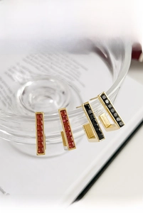 Detail of geometric gold earrings with red and black square-cut gemstones on glass