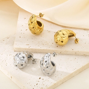 Detail of woven C-shaped stud earrings in gold and silver finish on a stone tray