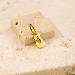 Detailed close-up of a polished gold letter J alphabet pendant on natural travertine stone