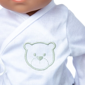 Detail of white cotton doll top featuring a cute green bear embroidery and cross collar