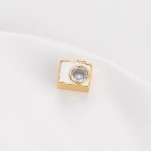 Dettaglio di un ciondolo a fotocamera dorata con smalto bianco e zircone scintillante