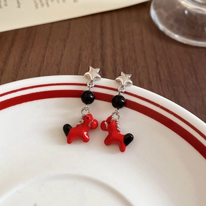 Close-up of red pony earrings with black beads and silver stars on ceramic tray