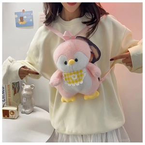 Pink plush penguin backpack with yellow plaid bib shown on a model in a cozy room