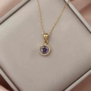 Macro shot of gold necklace with a purple zircon round pendant on a grey jewelry box