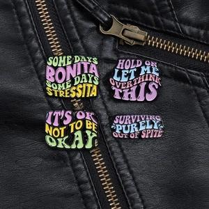 Gros plan de quatre pin's colorés en émail avec citations sur une veste en cuir noir à fermeture