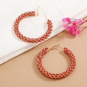 Detail of gold circle earrings with red rhinestones on white linen and dried flowers