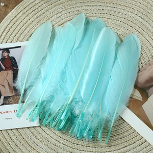 Flat lay of cyan goose feathers for DIY crafts on a woven mat with decorative card