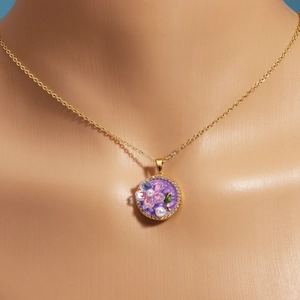 Macro shot of gold floral pendant with white pearls and purple oil painting style inlay