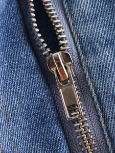 Macro view of metal zipper and blue denim fabric texture on a cropped jacket