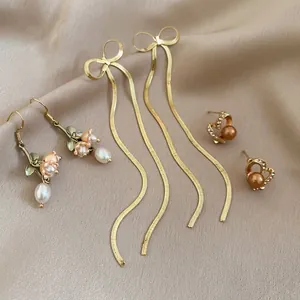 Elegant gold flower pearl earrings and long tassel stud set on soft beige silk background