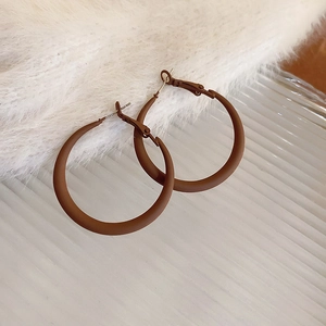 Detail view of matte brown hollow hoop earrings on soft plush and glass textures