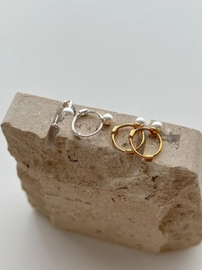Detailed close-up of gold and silver pearl hoop earrings on a natural stone base