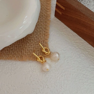 Elegant gold knot pearl earrings set on rustic linen and wood for a minimalist style
