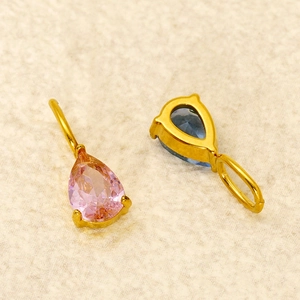 Macro detail of pear-shaped pink and blue zircon charms with golden steel settings