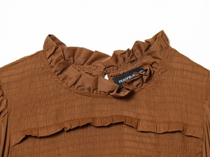 Detailed close-up of brown textured fabric with smocked details and ruffled neckline design
