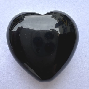 Polished black obsidian heart stone with glossy mirror finish on white surface